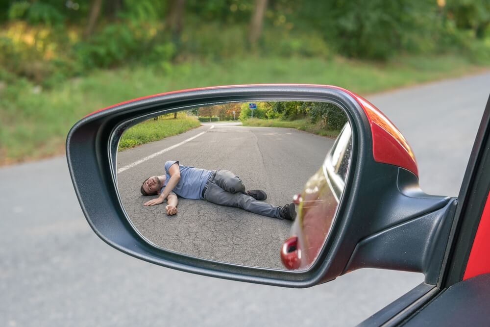 Injured man on road in rear mirror of a car.